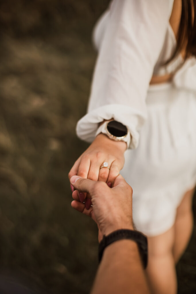 Close-up of hands holding with a white sleeve and watch visible, showing an engagement or wedding ring.