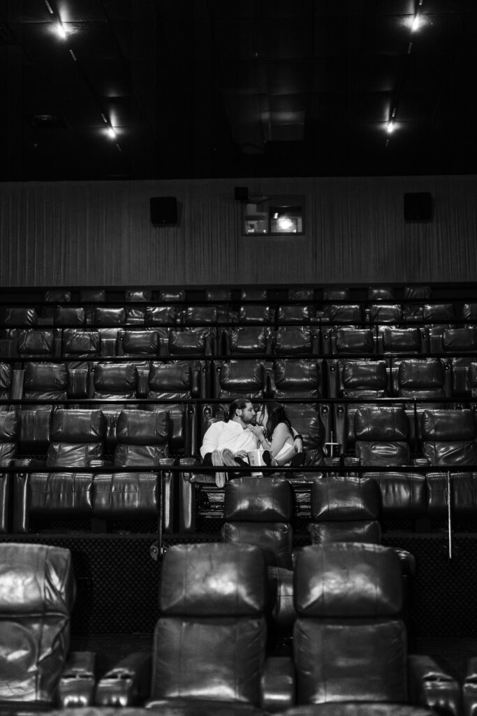 Man and women sitting inside a theater all alone sharing a kiss. 
