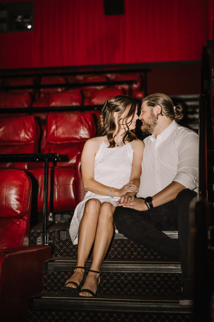 Man and women sitting a movie theater closely looking at each other. 